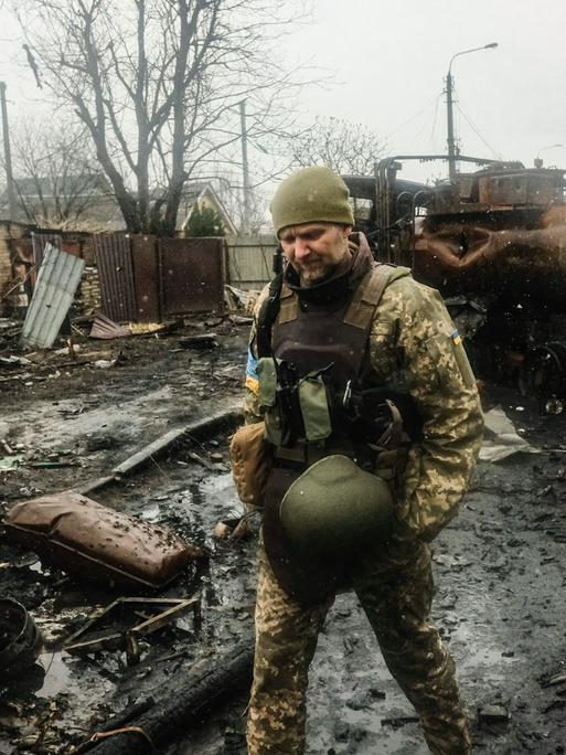 Ein ukrainischer Soldat läuft durch eine kriegsverwüstete Straße. Er inspiziert die Trümmer eines russischen Panzers.