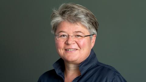 Portrait einer kurzhaarigen Frau mit Brille vor einem dunkelgrünen Hintergrund