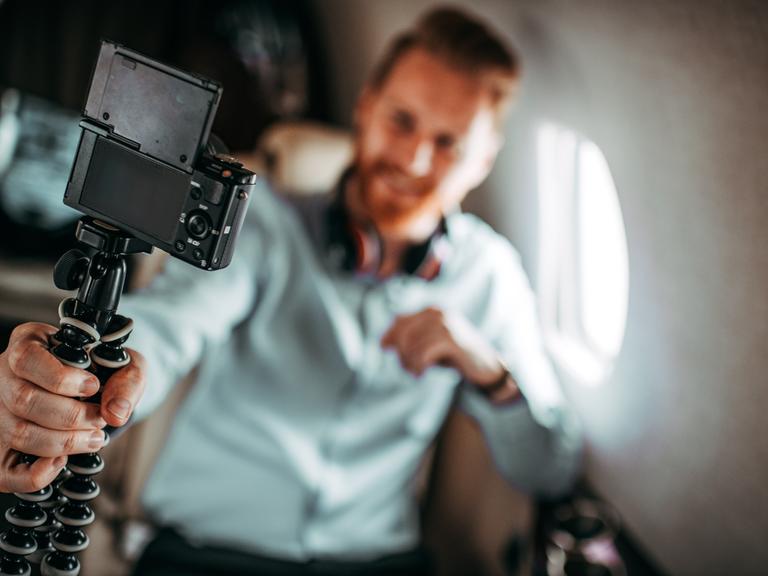 Eine Person mit einer Selfiekamera sitzt in einem Provatflugzeug und filmt sich.