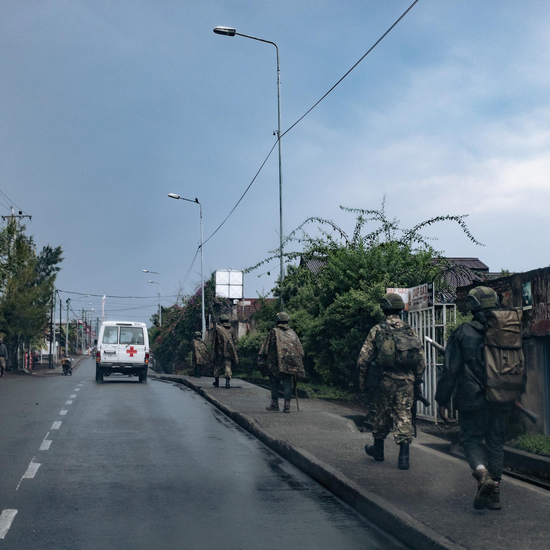Uniformierte und bewaffnete M23-Rebellen laufen hintereinander über einen Bürgersteig.