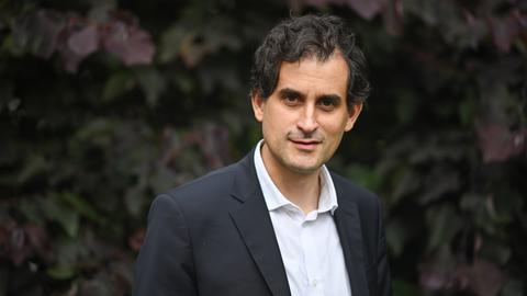 Philipp Peyman Engel steht in einem schwarzen Anzug mit weißem Hemd in einem Garten und schaut in die Kamera.