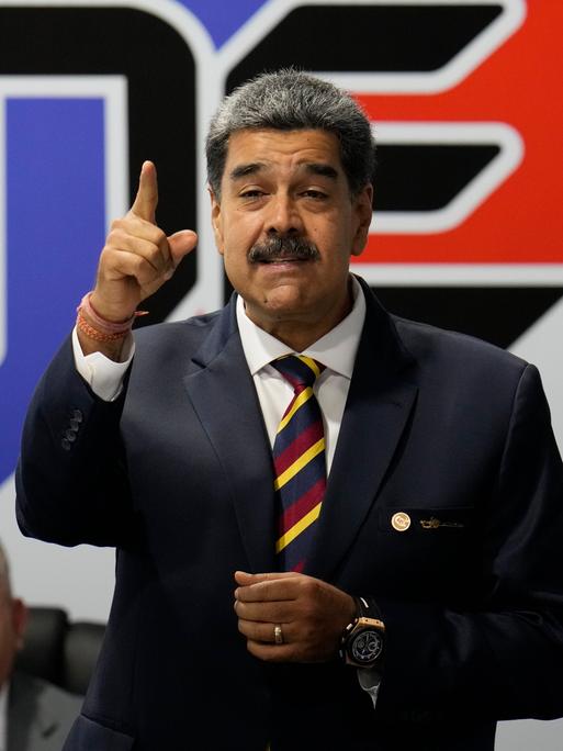 Präsident Nicolas Maduro trägt einen schwarzen Anzug und spricht gestikulierend.