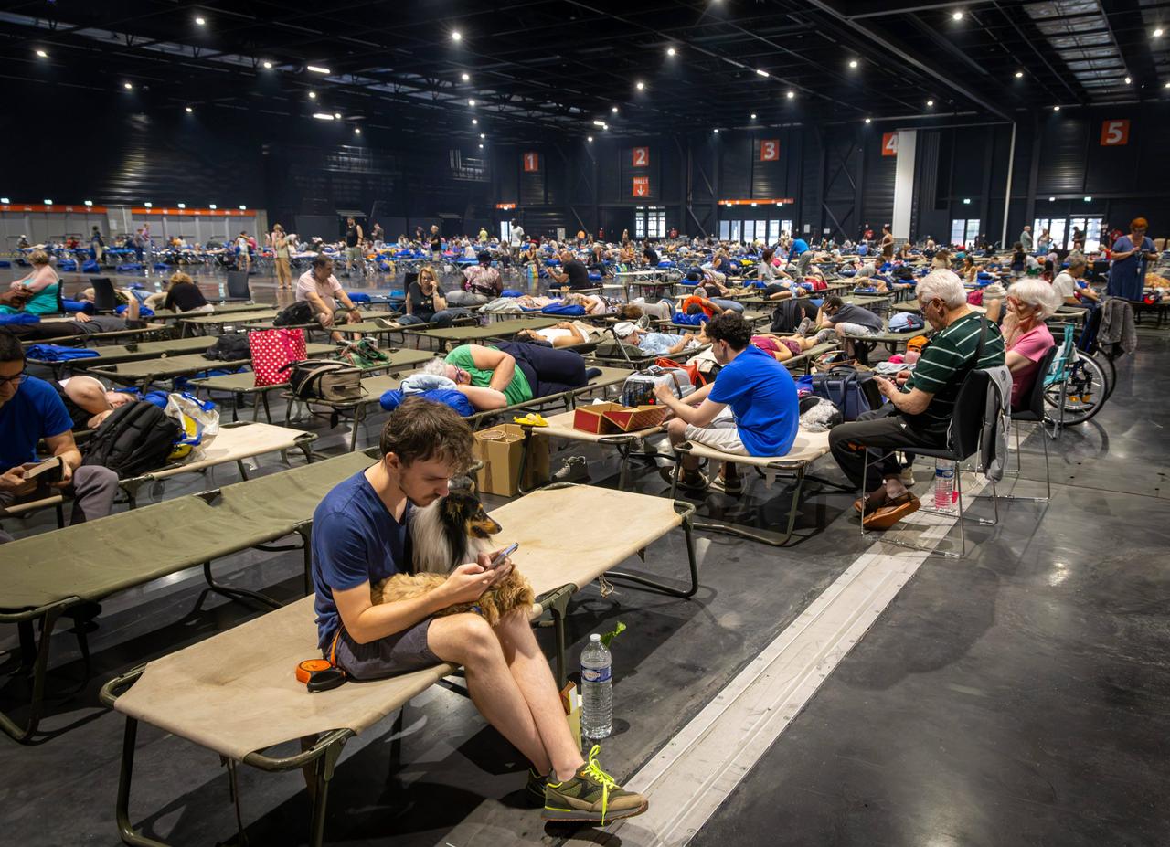 Das Foto zeigt eine Halle in Bordeaux, in der viele Menschen auf Feldbetten sitzen und liegen. Das Foto zeigt eine Halle in Bordeaux, in der viele Menschen auf Feldbetten sitzen und liegen.