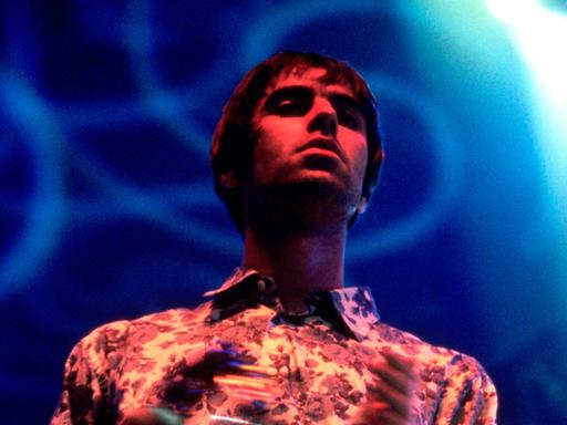 Liam Gallagher performt im November 1995 mit einem Schellenkranz auf einer grell lila-blau ausgeleuchteten Bühe mit Oasis live im Earls Court Exhibition Centre in London.