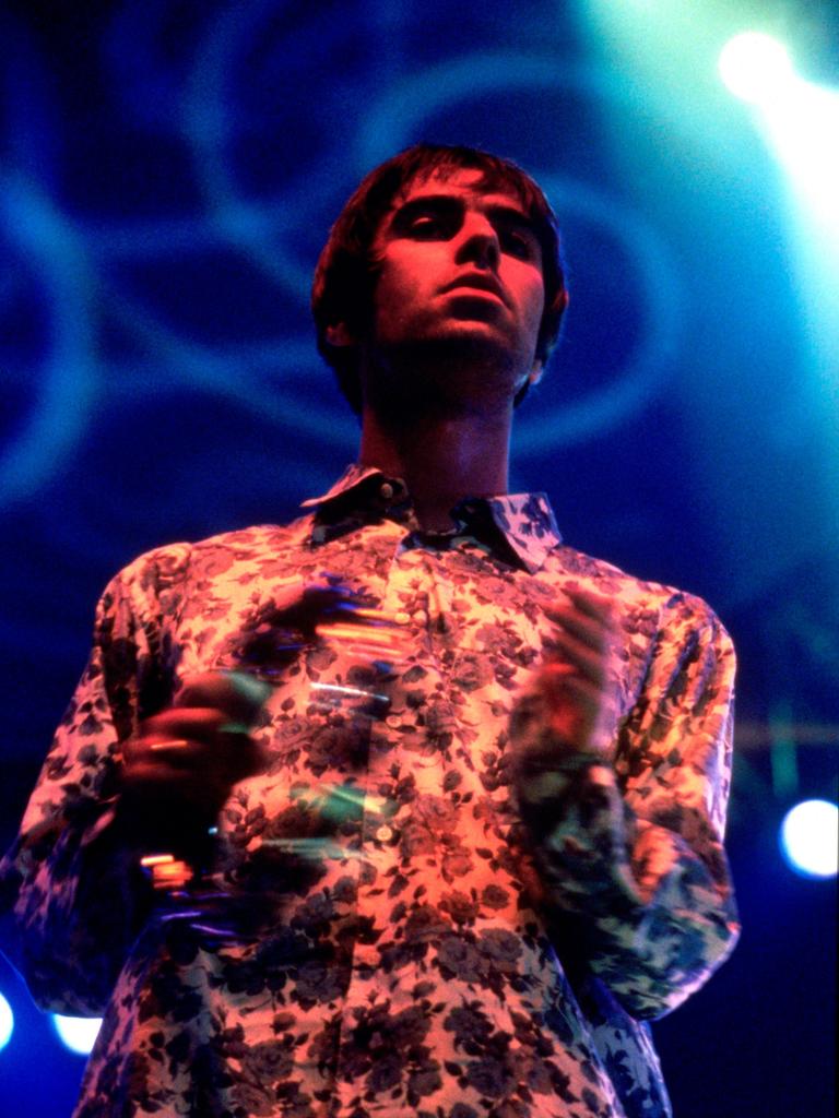 Liam Gallagher performt im November 1995 mit einem Schellenkranz auf einer grell lila-blau ausgeleuchteten Bühe mit Oasis live im Earls Court Exhibition Centre in London.
