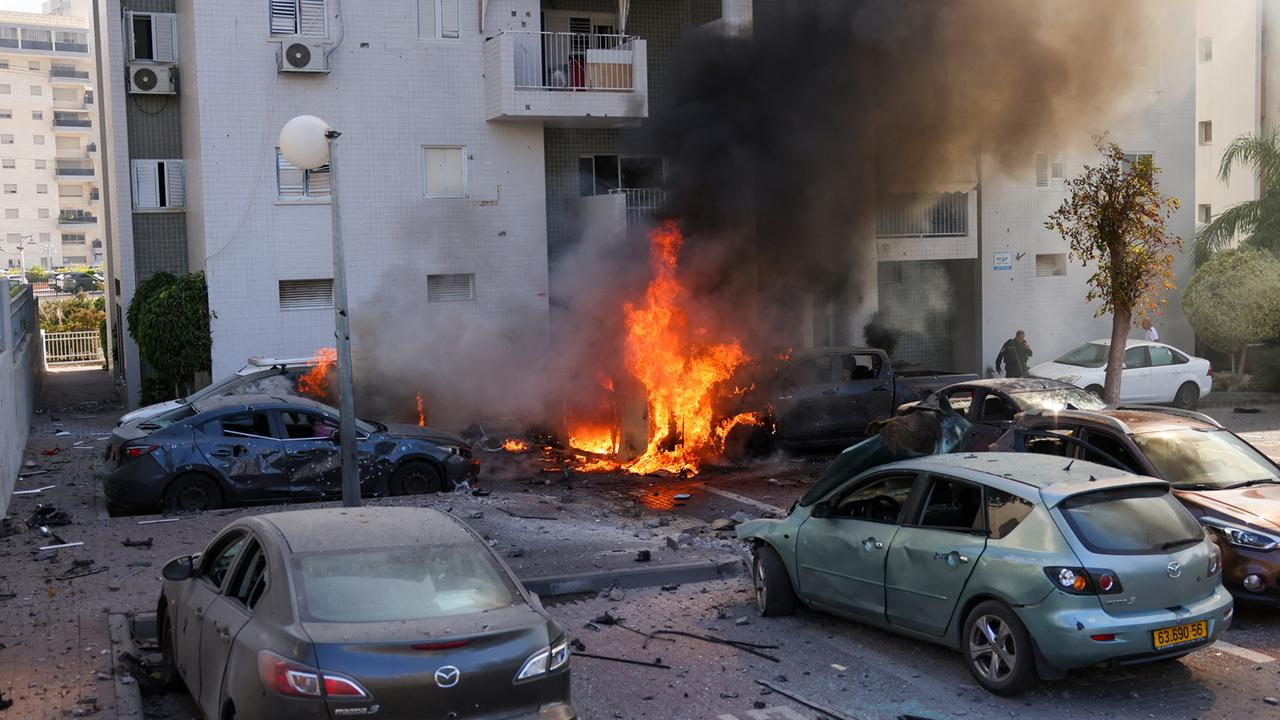 Feuer vor einem Wohnhaus, ein Mitglied der israelischen Sicherheitskräfte steht in der Nähe brennender Autos nach einem Raketenangriff aus dem Gazastreifen in Aschkelon, Südisrael, am 7. Oktober 2023. 