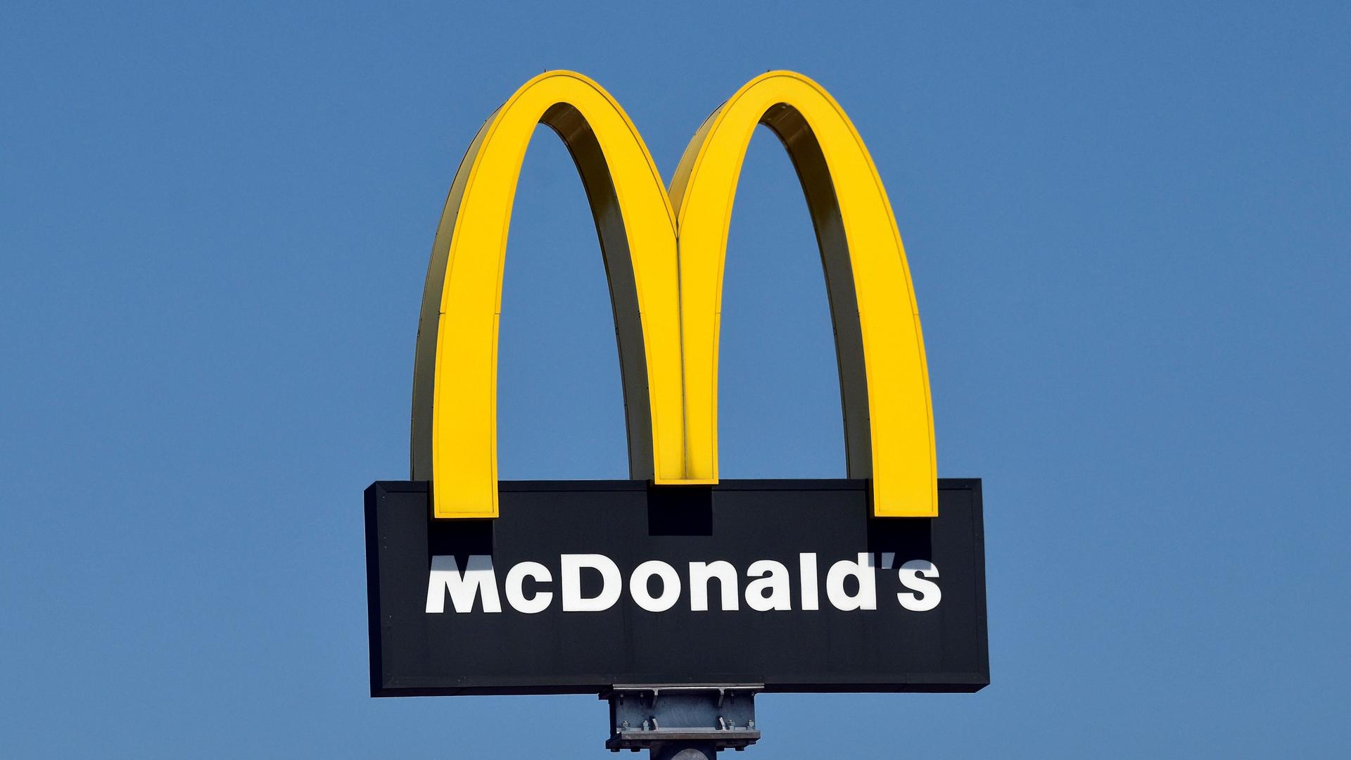 Logo der Firma McDonalds auf einem Metallpfahl vor blauem Himmel.