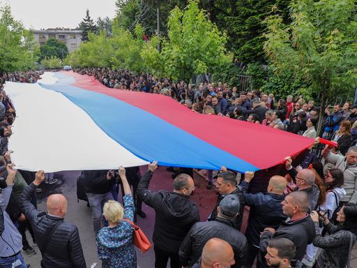 Menschen halten eine riesige serbische Flagge während ihres Protestes hoch.
