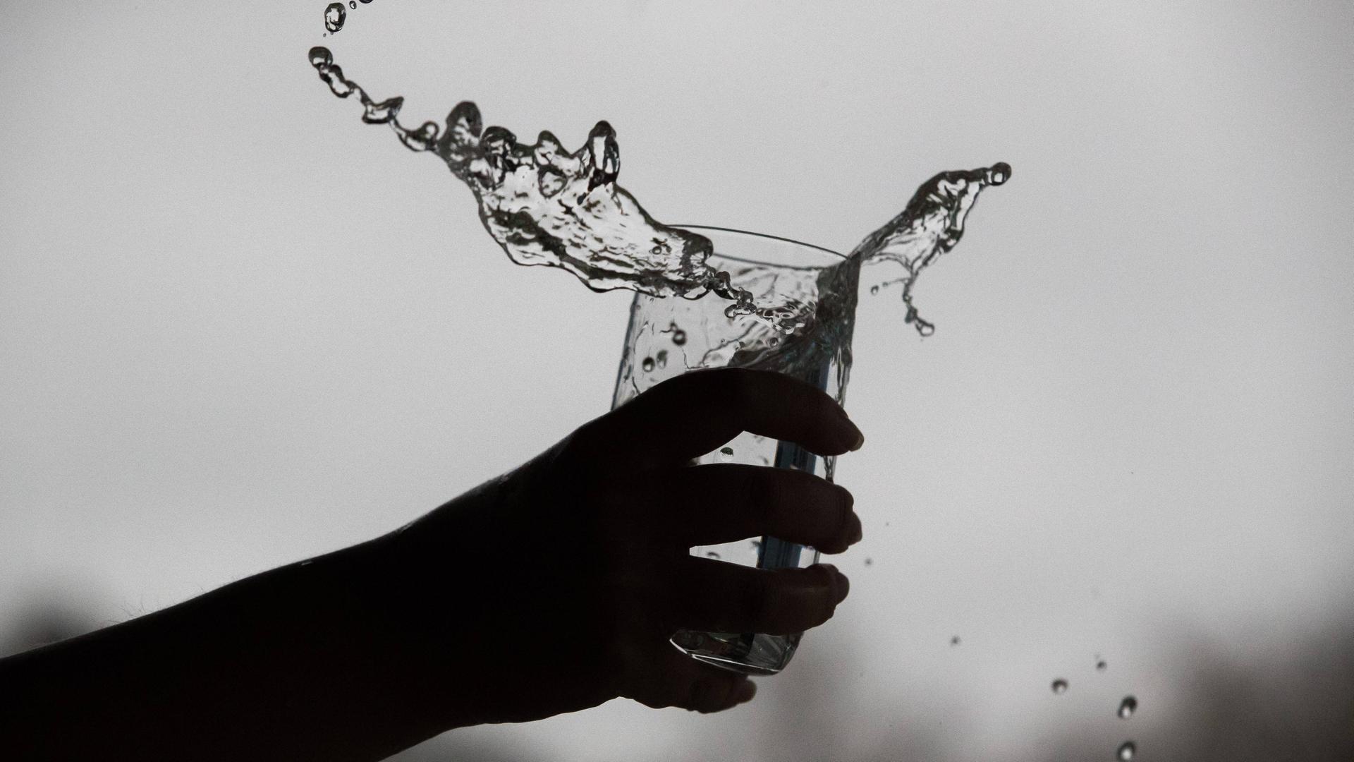 Eine zitternde Hand lässt Wasser aus einem Glas überschwappen.