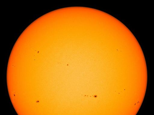 Eine Teleskop-Total-Aufnahme der Sonne zeigt verschiedene unregelmäßig verteilte, dunkle Flecken