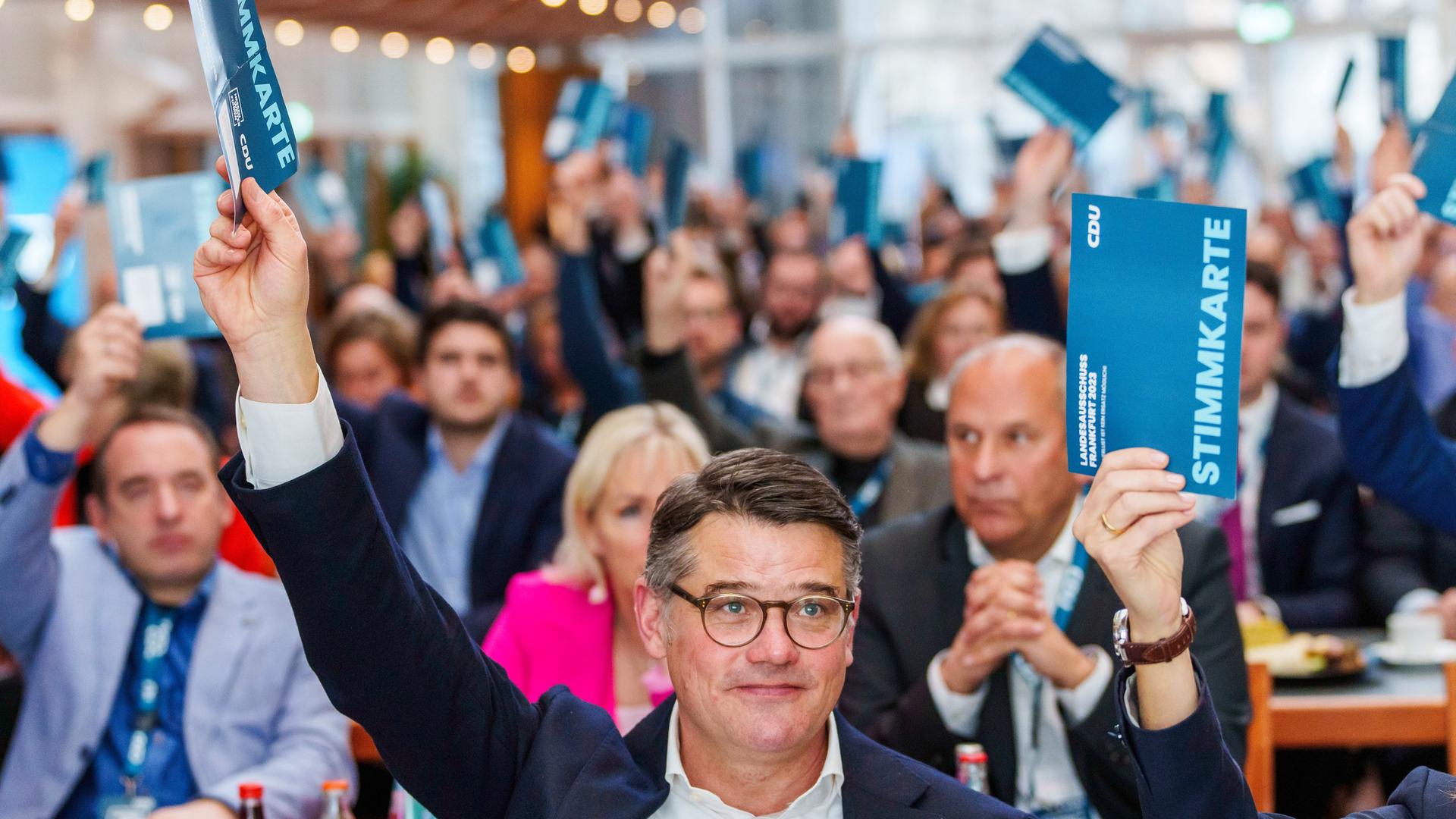Boris Rhein (CDU, vorne), Ministerpräsident von Hessen, hebt seine Stimmkarte und votiert für den Koalitionsvertrag. Im Hintergrund heben weitere Delegierte die Stimmkarten in die Luft.