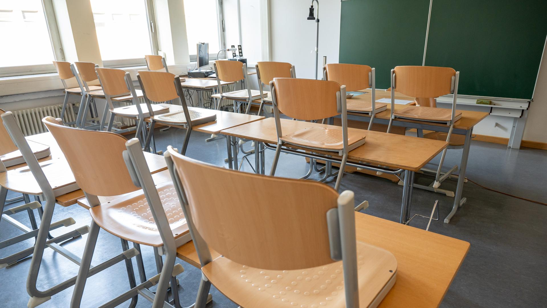 Ein leeres Klassenzimmer mit hochgestellten Stühlen und einer grünen Tafel im Hintergrund.