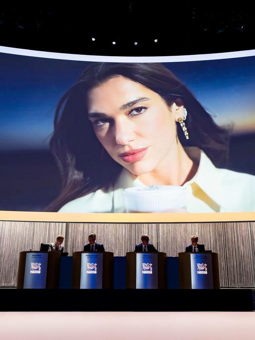 Ein großer Bildschirm mit einem Bild von Dua Lipa bei der Vorstellung der Werbekampagne für Nespresso