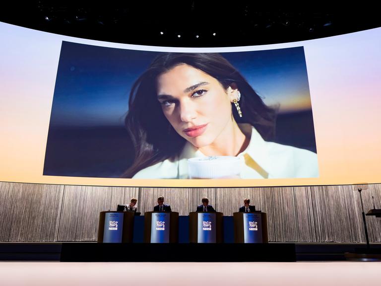 Ein großer Bildschirm mit einem Bild von Dua Lipa bei der Vorstellung der Werbekampagne für Nespresso
