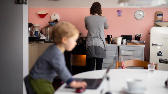 Das Foto zeigt eine Frau in der Küche, ihr Kleinkind steht auf einem Stuhl vor einem Computer