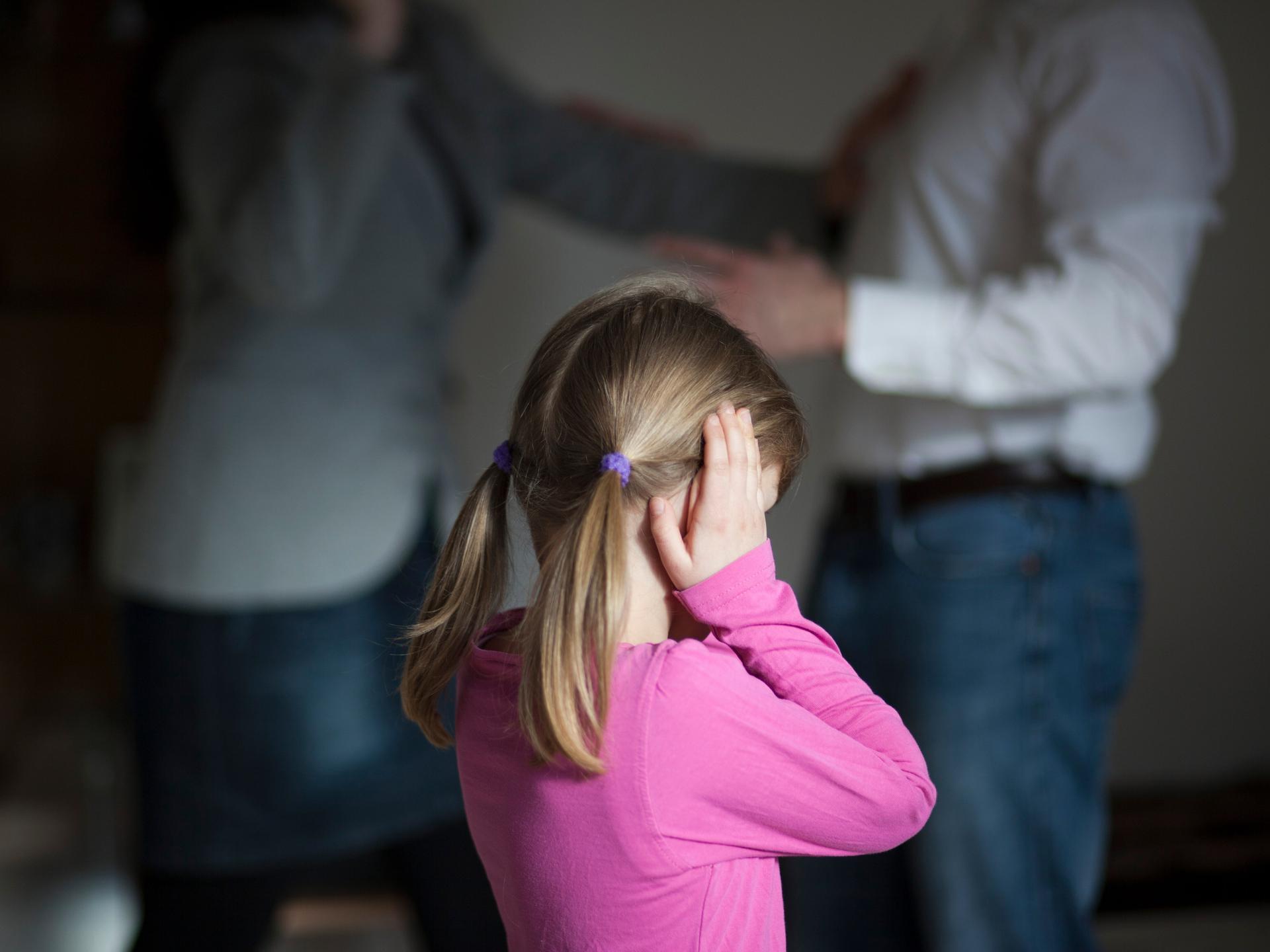 Zwei Erwachsene streiten sich, während die Tochter dazwischen steht und sich die Ohren zuhält. 