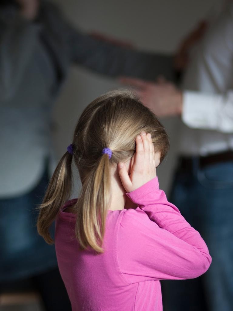 Zwei Erwachsene streiten sich, während die Tochter dazwischen steht und sich die Ohren zuhält. 