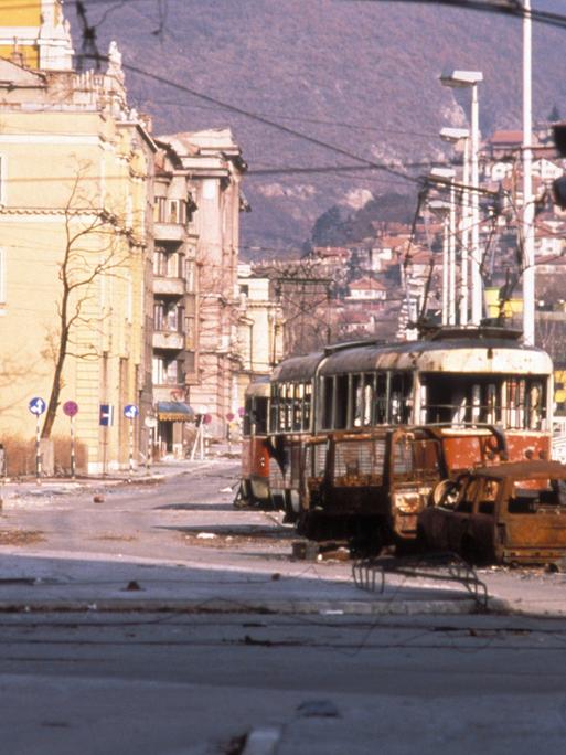 Straße mit zerstörten Straßenbahnwaggons und Autos in Sarajevo 1993.
