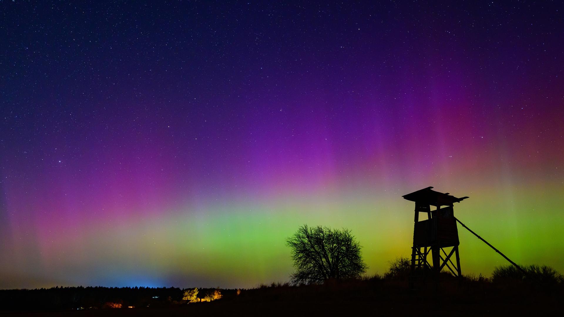 Vor dem grün und violett erleuchteten Nachthimmel zeichnet sich die Silhouette eines Hochstands ab.