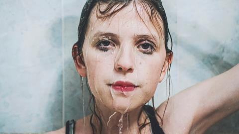 Eine junge Frau schaut traurig, Wasser rinnt über ihr Gesicht.