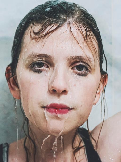 Eine junge Frau schaut traurig, Wasser rinnt über ihr Gesicht.