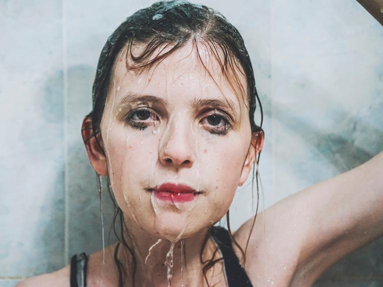 Eine junge Frau schaut traurig, Wasser rinnt über ihr Gesicht.