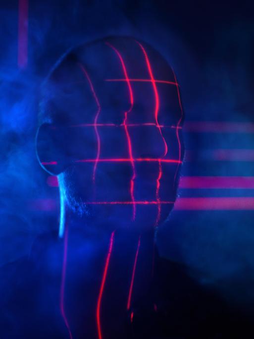 Rotes Licht wirft ein biometrisches Raster auf den verschatteten Kopf eines Mannes.