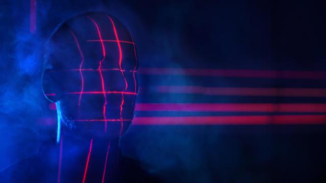 Rotes Licht wirft ein biometrisches Raster auf den verschatteten Kopf eines Mannes.