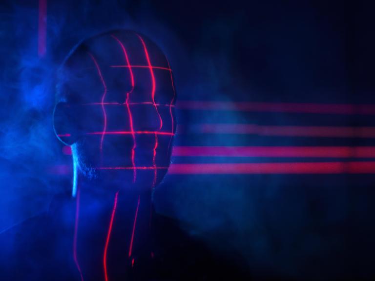 Rotes Licht wirft ein biometrisches Raster auf den verschatteten Kopf eines Mannes.