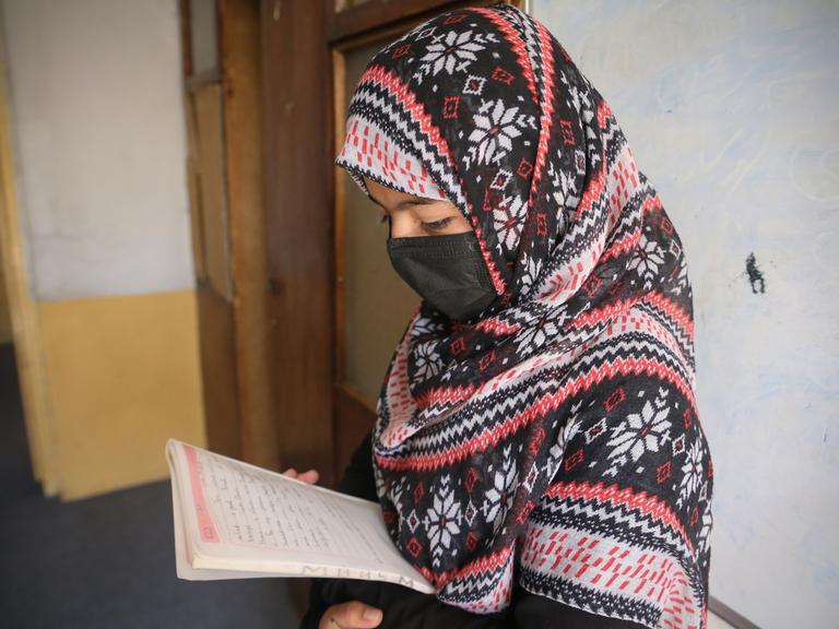 Eine junge afghanische Frau mit Kopftuch blickt in ein beschriebenes Heft.