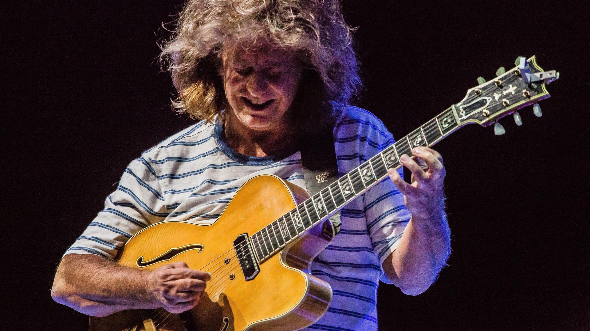 Wir sehen den Gitarristen Pat Metheny, wie er während eines Konzerts seine Gitarre spielt. 