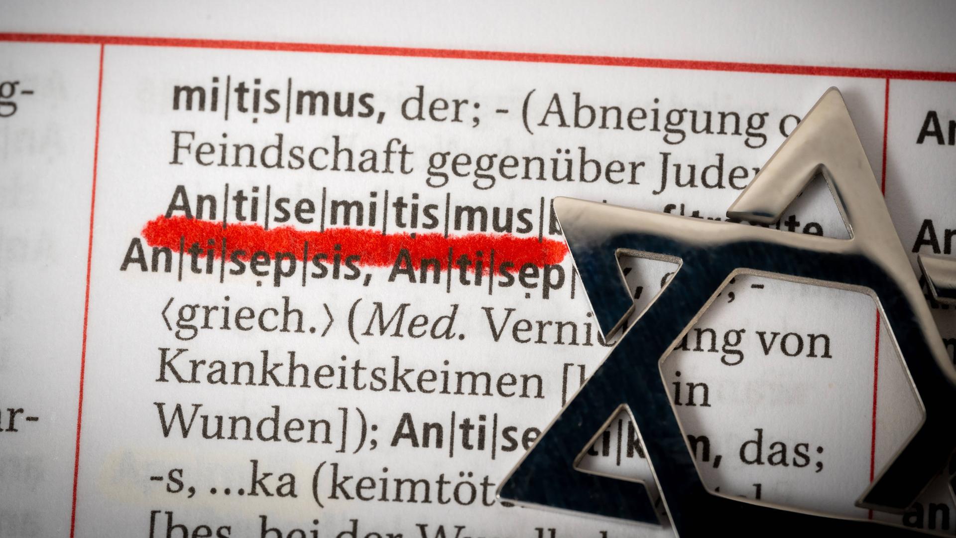 In einem Wörterbuch ist das Wort "Antisemitismus" rot unterstrichen. Daneben liegt ein Davidstern