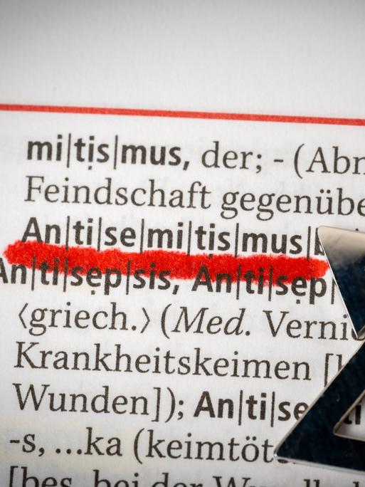 In einem Wörterbuch ist das Wort "Antisemitismus" rot unterstrichen. Daneben liegt ein Davidstern