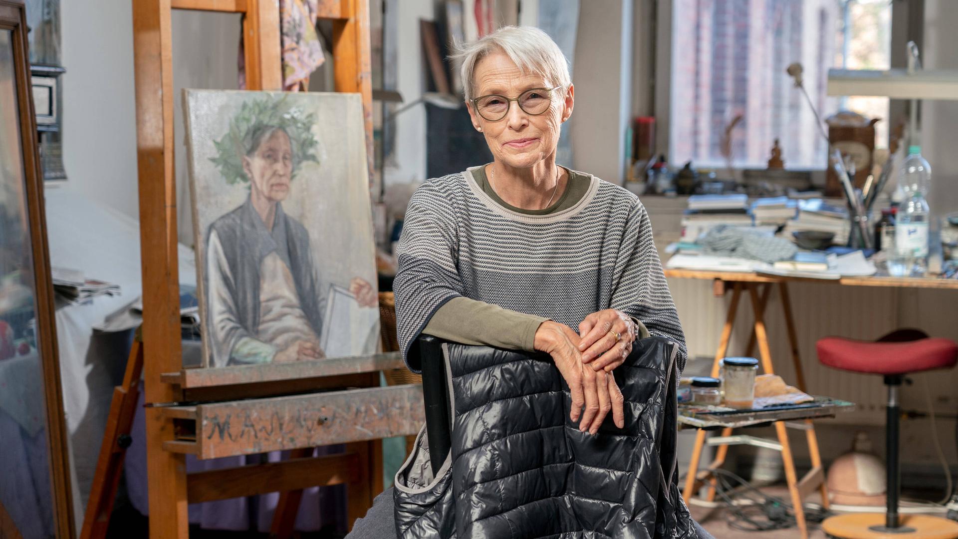 Die Leipziger Malerin Doris Ziegler in ihrem Atelier im Stadteil Plagwitz. Sie schaut in die Kamera. Im Hintergrund ist ihre Malerei zu sehen.