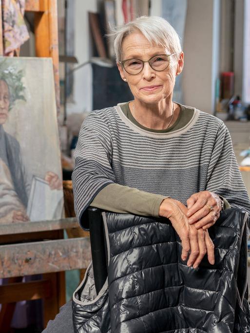 Die Leipziger Malerin Doris Ziegler in ihrem Atelier im Stadteil Plagwitz. Sie schaut in die Kamera. Im Hintergrund ist ihre Malerei zu sehen.