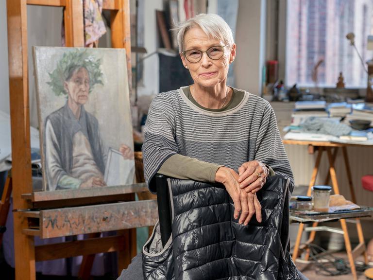 Die Leipziger Malerin Doris Ziegler in ihrem Atelier im Stadteil Plagwitz. Sie schaut in die Kamera. Im Hintergrund ist ihre Malerei zu sehen.