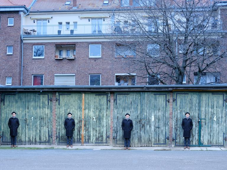 Eine Bildmontage von einem Mann mit Hut, der vier Mal vor einer reighe von vier Garagentoren steht