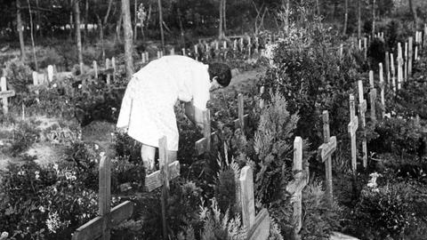 Altes Schwarz-Weiß-Foto einer Frau, die sich auf dem Friedhof von Oksbøl über ein Grab beugt.