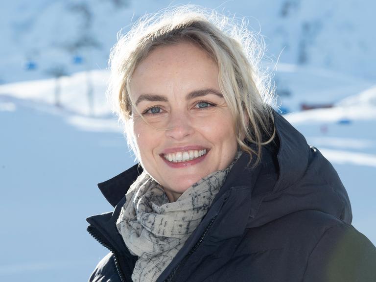 Nina Hoss steht freundlich lachend in einer Schneelandschaft
