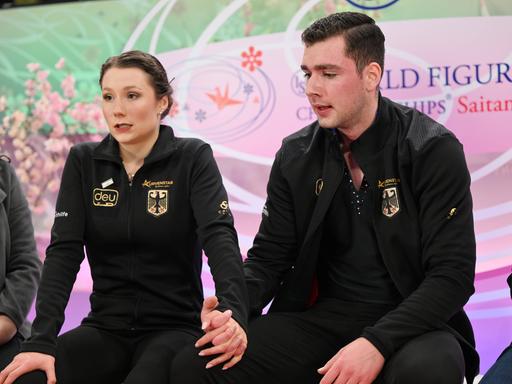 Das Eiskunstlaufpaar Annika Hocke und Robert Kunkel warten bei den Weltmeisterschaften 2023 in Saitama auf ihre Wertnoten. Dabei halten sie sich an den Händen. 