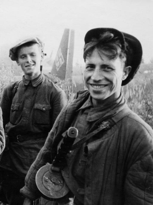 Vier junge Partisanen grinsen vor einem Flugzeug der Nazis in die Kamera