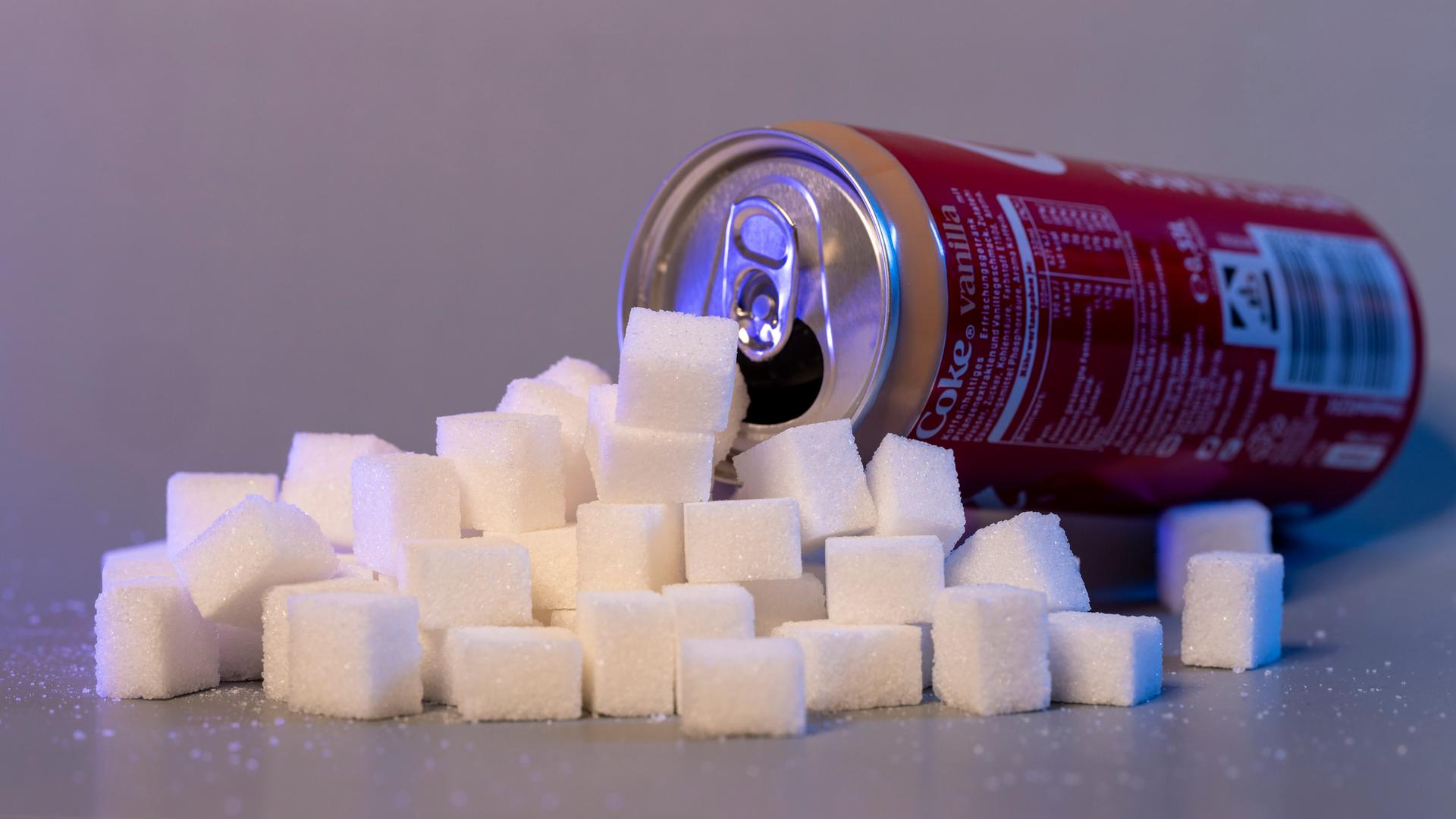 Ein Berg von Zuckerwürfeln liegt vor einer leeren Cola-Dose. Ein Berg von Zuckerwürfeln liegt vor einer leeren Cola-Dose.