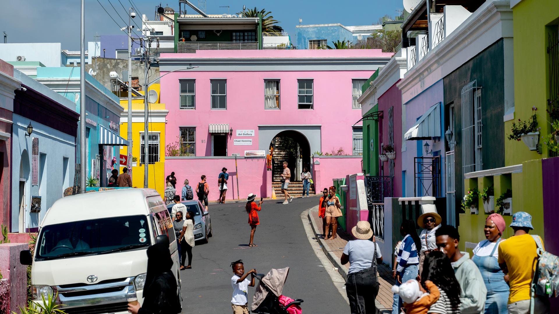 Bunte Häuser stehen im Stadtviertel Bo-Kaap in Kapstadt/Südafrika, viele Menschen laufen auf der Straße. Der Stadtteil entstand als Siedlung von Kapmalaien, die bis heute die Mehrheit der Bewohner stellen. Bunte Häuser stehen im Stadtviertel Bo-Kaap in Kapstadt/Südafrika, viele Menschen laufen auf der Straße. Der Stadtteil entstand als Siedlung von Kapmalaien, die bis heute die Mehrheit der Bewohner stellen.