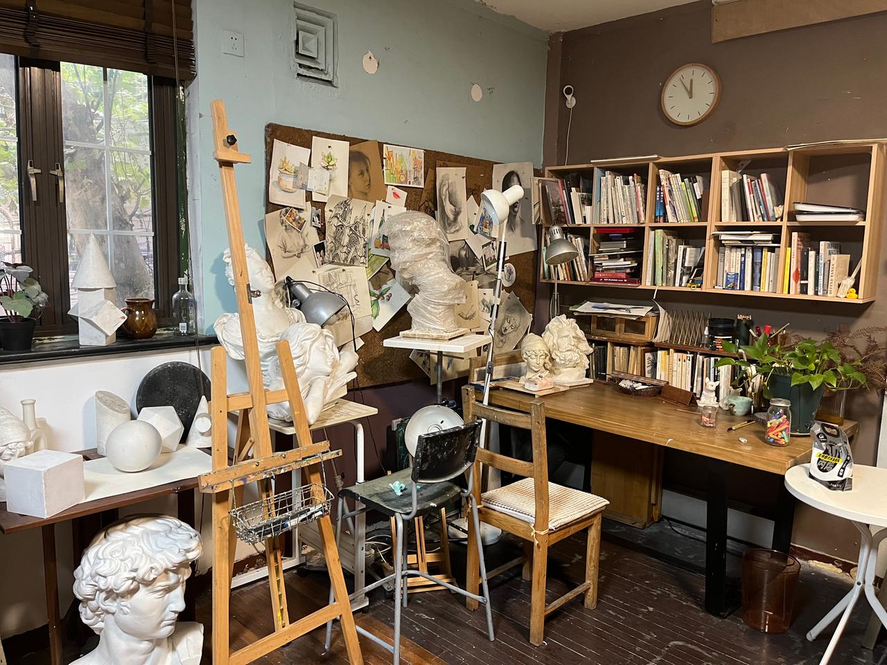 Ein Atelier mit Staffelei, Skulpturen und vielen Büchern im Regal.