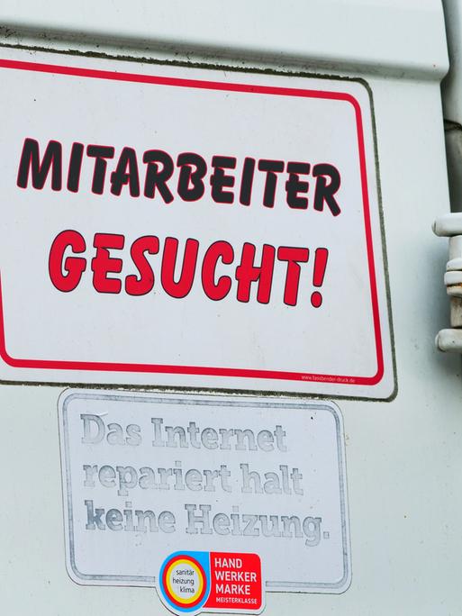 "Mitarbeiter gesucht!" steht auf einem Schild am Transporter eines Handwerksbetriebs für Heizung und Sanitär.