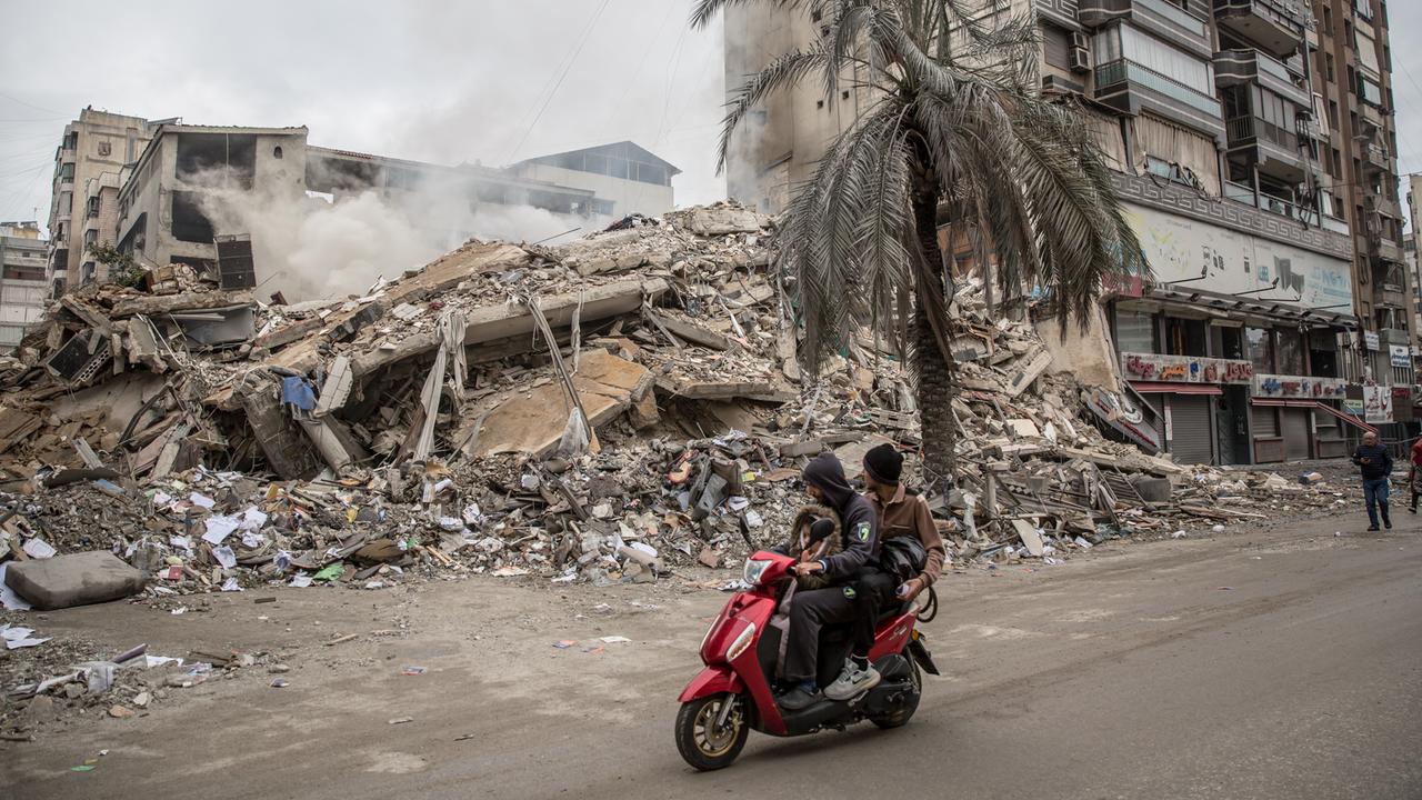 Ein zerstörtes Haus in Beirut. Jemand fährt auf einem roten Motorroller vorbei.