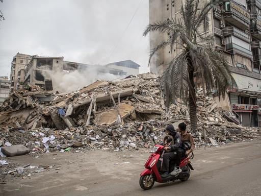 Ein zerstörtes Haus in Beirut. Jemand fährt auf einem roten Motorroller vorbei.