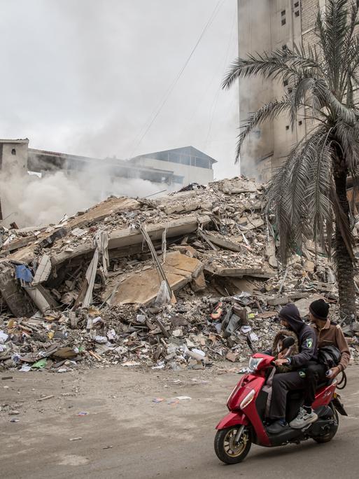 Ein zerstörtes Haus in Beirut. Jemand fährt auf einem roten Motorroller vorbei.