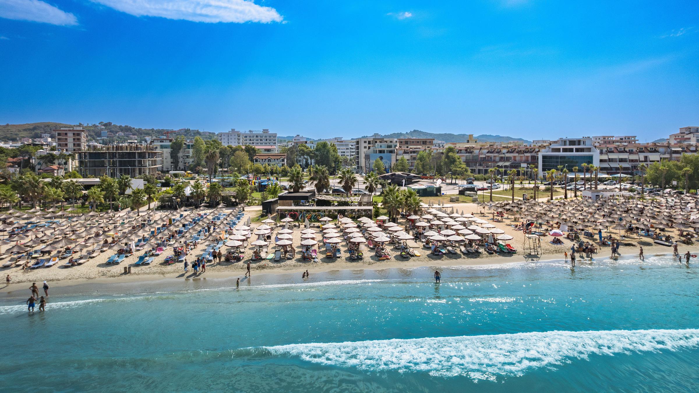 Blick auf einen Strand in Albanien, an dem tausende Sonnenschirme aufgespannt sind und zahlreich Touristen baden.