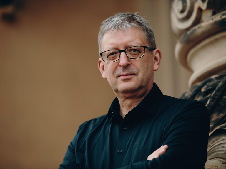 Hans-Christoph Rademann steht neben einer barocken Fassade und schaut freundlich in die Kamera.